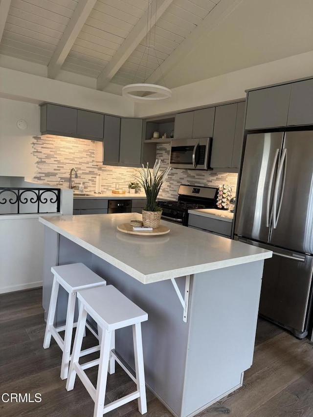 kitchen featuring gray cabinetry, a kitchen breakfast bar, light countertops, appliances with stainless steel finishes, and a center island