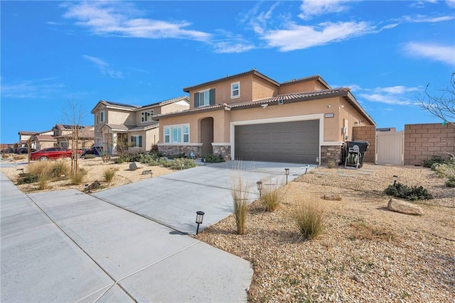 view of front of house featuring stucco siding, an attached garage, fence, stone siding, and driveway