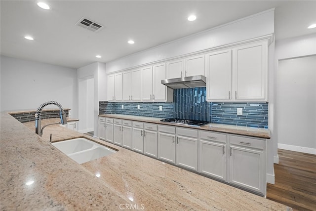 kitchen with sink, white cabinets, decorative backsplash, stainless steel gas cooktop, and light stone counters