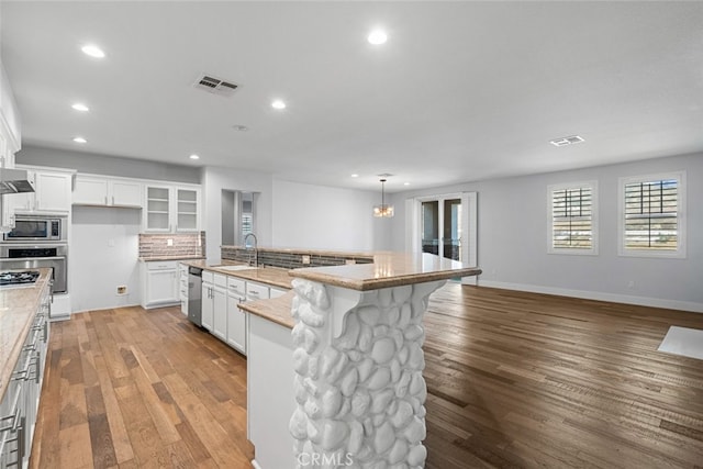 kitchen with light stone counters, hanging light fixtures, a center island with sink, appliances with stainless steel finishes, and white cabinets