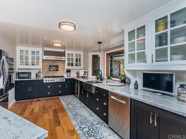 kitchen featuring decorative light fixtures, sink, white cabinets, stainless steel appliances, and wall chimney range hood