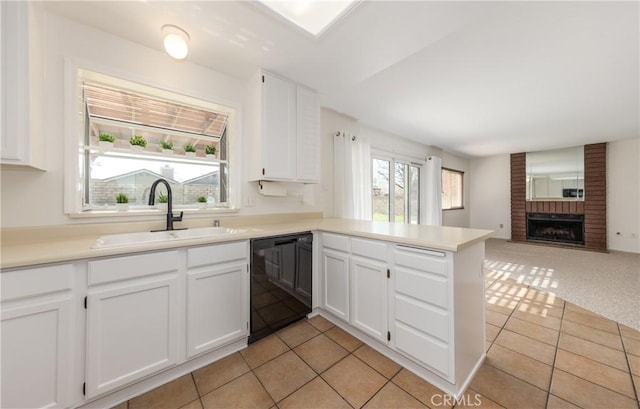 kitchen with a fireplace, white cabinetry, black dishwasher, sink, and kitchen peninsula