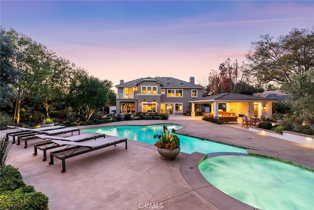 pool at dusk featuring an in ground hot tub, an outdoor living space, and a patio