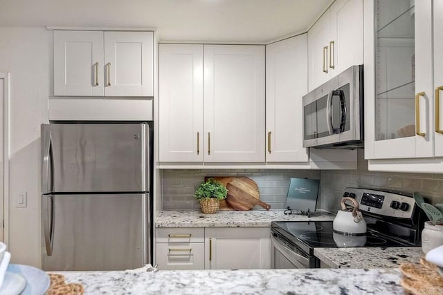 kitchen featuring backsplash, glass insert cabinets, light stone counters, white cabinets, and stainless steel appliances