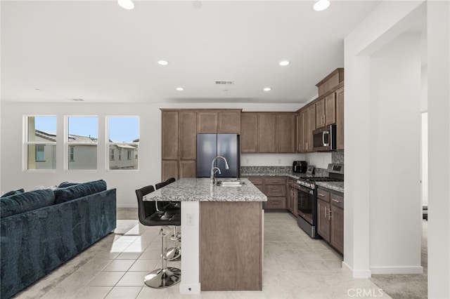 kitchen featuring light stone counters, a center island with sink, stainless steel appliances, open floor plan, and a kitchen breakfast bar