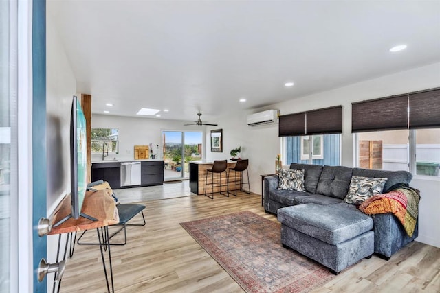 living room featuring ceiling fan, sink, light hardwood / wood-style flooring, and an AC wall unit