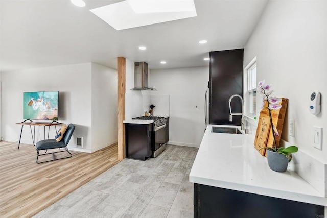 kitchen featuring sink, a skylight, gas range, wall chimney exhaust hood, and light wood-type flooring