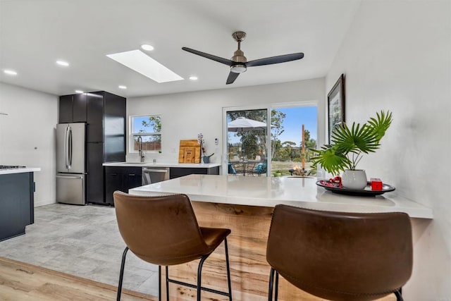 kitchen with sink, a skylight, a kitchen breakfast bar, kitchen peninsula, and stainless steel appliances