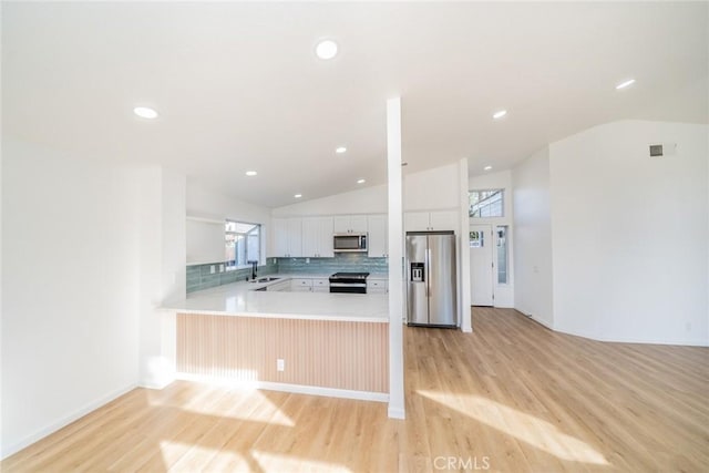 kitchen with lofted ceiling, appliances with stainless steel finishes, white cabinets, and kitchen peninsula