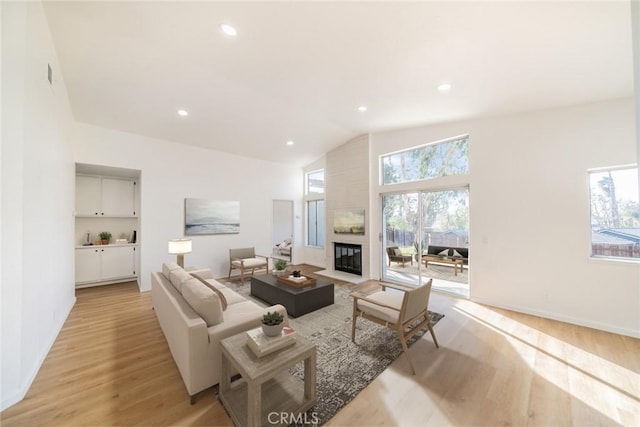 living room featuring high vaulted ceiling, a fireplace, light hardwood / wood-style floors, and a healthy amount of sunlight