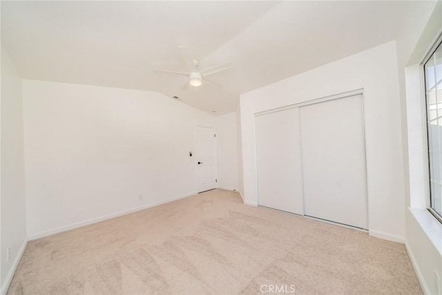 unfurnished bedroom with ceiling fan, a closet, vaulted ceiling, and light carpet