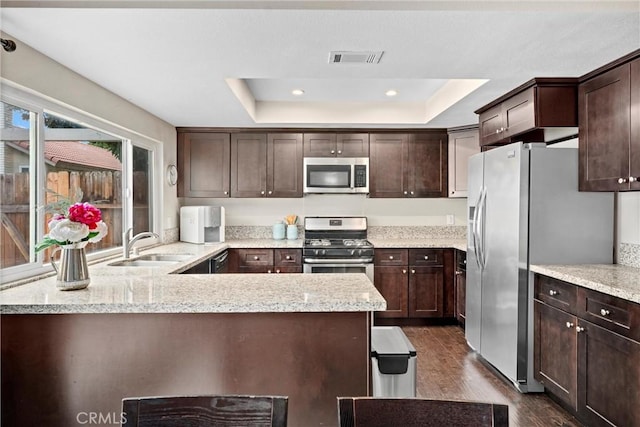 kitchen featuring a raised ceiling, light stone countertops, appliances with stainless steel finishes, and dark brown cabinetry