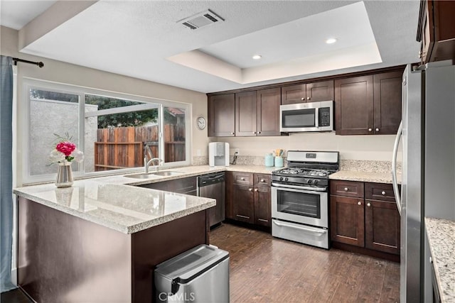 kitchen with stainless steel appliances, a raised ceiling, sink, and light stone counters