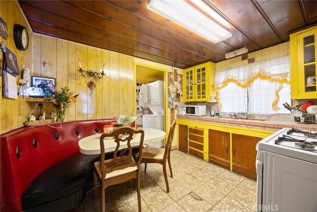 kitchen featuring wood walls, sink, stacked washer and dryer, wooden ceiling, and white appliances