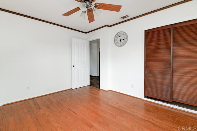 unfurnished bedroom featuring hardwood / wood-style flooring, crown molding, ceiling fan, and a closet