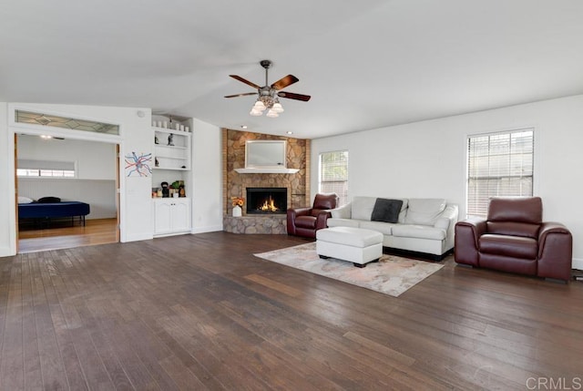 living area featuring dark wood-type flooring, built in features, a fireplace, lofted ceiling, and ceiling fan