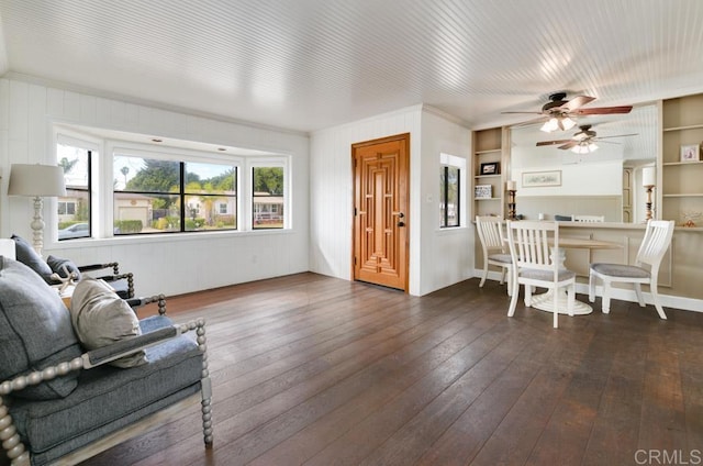 living area featuring dark wood-type flooring, built in shelves, and ceiling fan