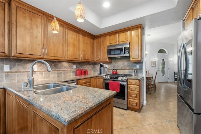 kitchen with sink, decorative light fixtures, appliances with stainless steel finishes, a tray ceiling, and light stone countertops