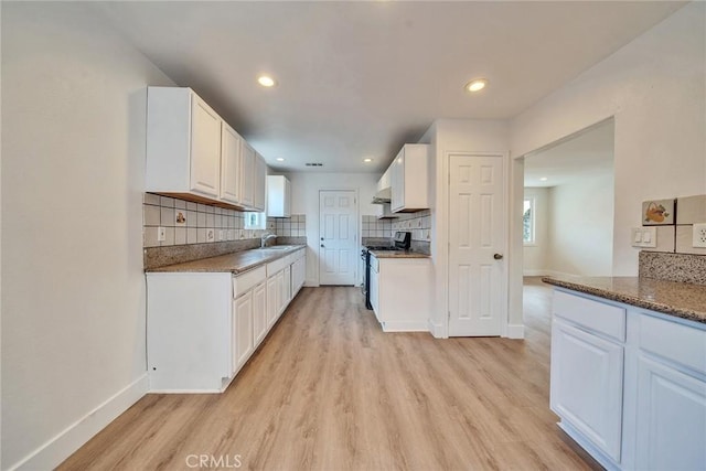 kitchen with stainless steel gas stove, sink, white cabinets, backsplash, and light hardwood / wood-style flooring