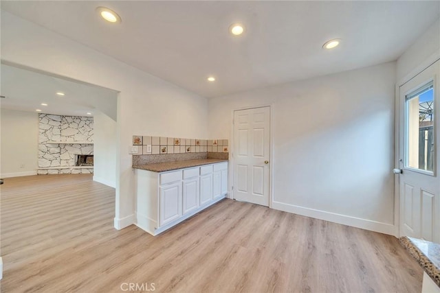 kitchen with backsplash, white cabinets, light hardwood / wood-style floors, and a fireplace