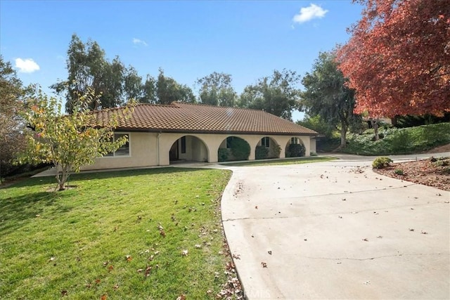 mediterranean / spanish home featuring a front yard, a tile roof, driveway, and stucco siding