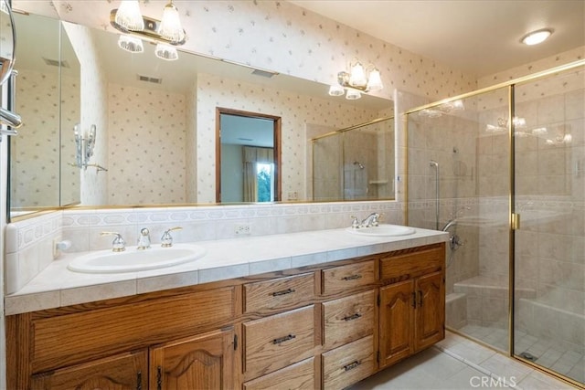 bathroom with a shower stall, double vanity, a sink, and wallpapered walls