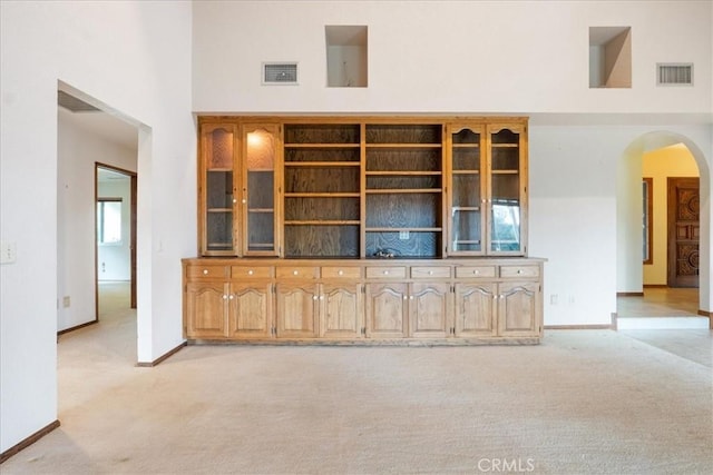 unfurnished living room featuring arched walkways, visible vents, a towering ceiling, and light colored carpet