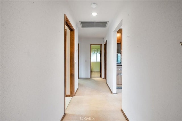 hallway with visible vents, light carpet, and baseboards