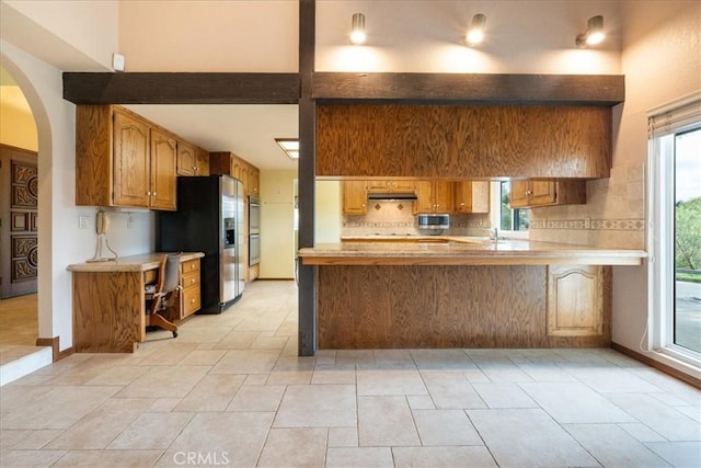 kitchen featuring under cabinet range hood, stainless steel appliances, a peninsula, light countertops, and brown cabinets