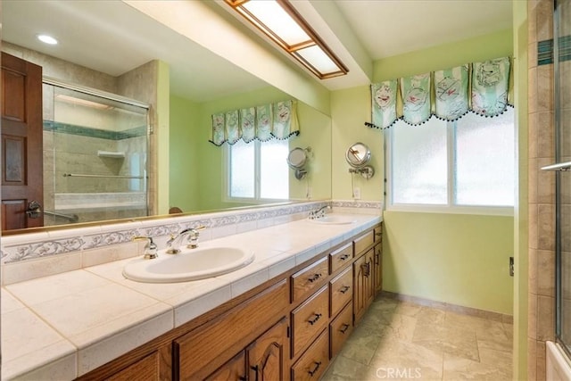 full bath featuring tiled shower, a sink, baseboards, and double vanity