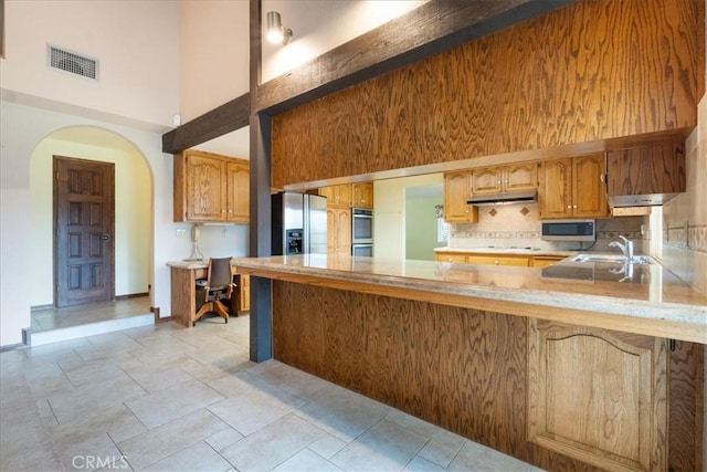 kitchen with a peninsula, a high ceiling, appliances with stainless steel finishes, and light countertops