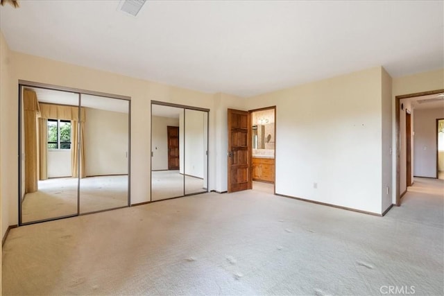 unfurnished bedroom featuring multiple closets, light colored carpet, visible vents, ensuite bath, and baseboards