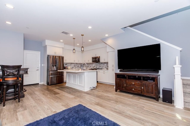 kitchen with decorative light fixtures, appliances with stainless steel finishes, a kitchen island with sink, light hardwood / wood-style floors, and backsplash