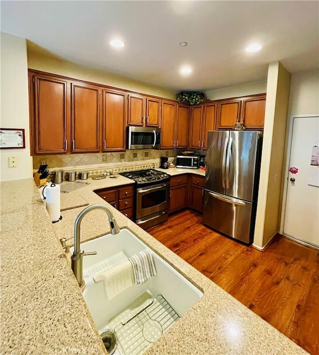 kitchen featuring dark hardwood / wood-style flooring, light stone countertops, stainless steel appliances, and sink