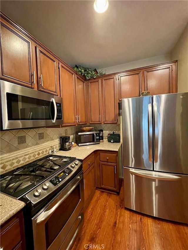 kitchen featuring light stone countertops, decorative backsplash, light hardwood / wood-style floors, and appliances with stainless steel finishes