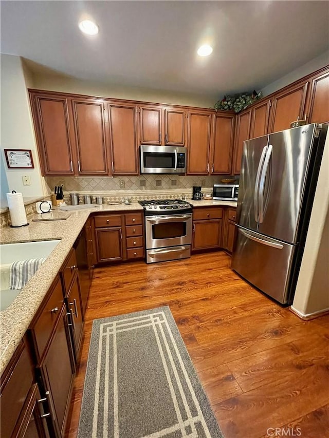 kitchen featuring sink, light stone counters, light hardwood / wood-style flooring, stainless steel appliances, and decorative backsplash