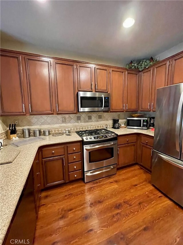 kitchen with appliances with stainless steel finishes, light stone countertops, hardwood / wood-style floors, and decorative backsplash