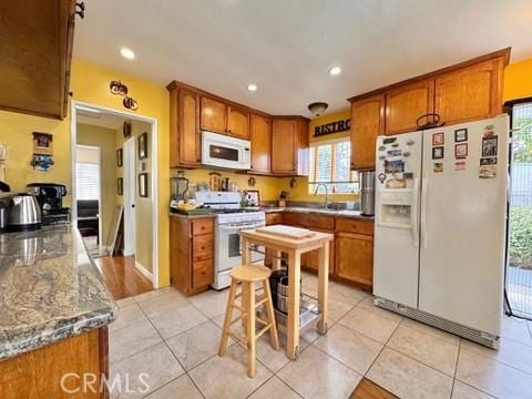 kitchen with light stone counters, light tile patterned floors, white appliances, and a kitchen breakfast bar