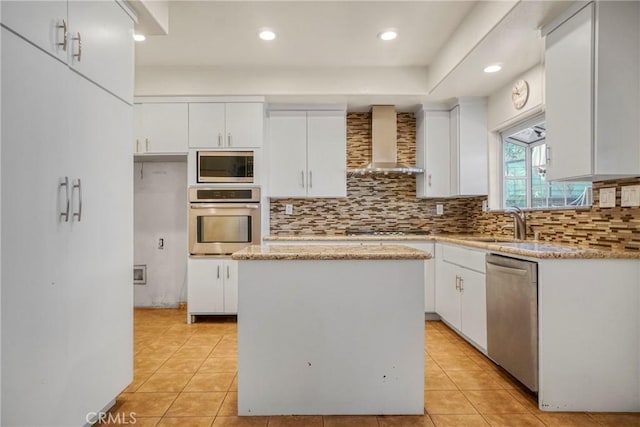 kitchen featuring wall chimney exhaust hood, white cabinetry, appliances with stainless steel finishes, and a center island