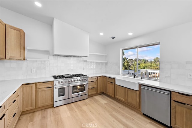 kitchen with tasteful backsplash, stainless steel appliances, sink, and light hardwood / wood-style flooring