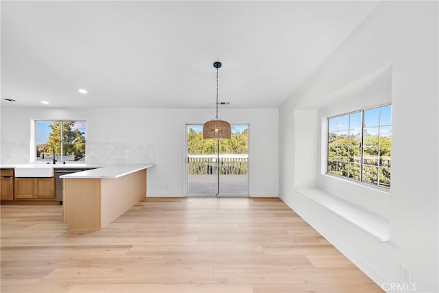 kitchen featuring sink, decorative light fixtures, light hardwood / wood-style flooring, kitchen peninsula, and a wealth of natural light