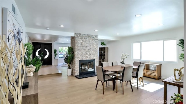 dining room featuring a stone fireplace, a wealth of natural light, and light wood-type flooring