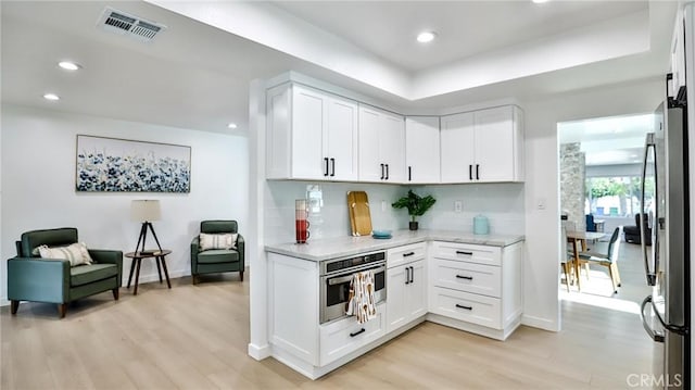 kitchen with light hardwood / wood-style flooring, stainless steel appliances, light stone countertops, white cabinets, and decorative backsplash