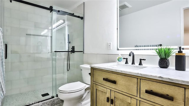 bathroom with vanity, a shower with door, tile walls, and toilet