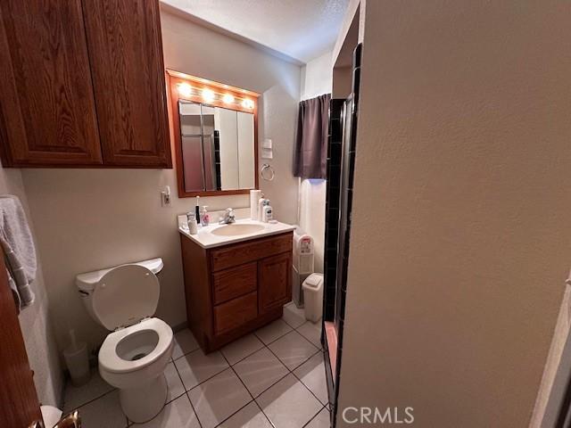 bathroom featuring walk in shower, vanity, toilet, and tile patterned flooring