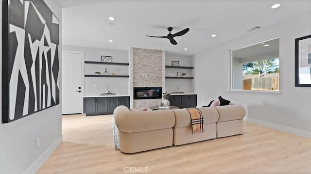 living room featuring ceiling fan, a stone fireplace, light wood-type flooring, and built in shelves