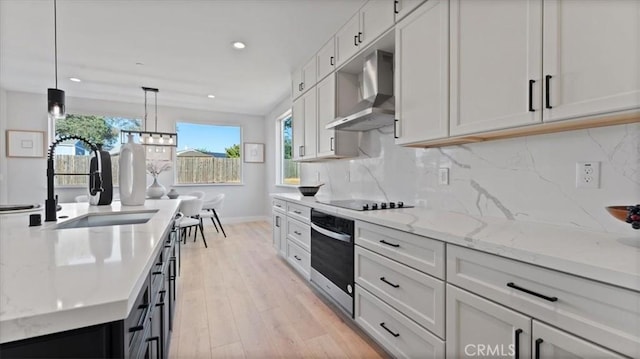 kitchen featuring sink, hanging light fixtures, black electric cooktop, wall oven, and wall chimney range hood