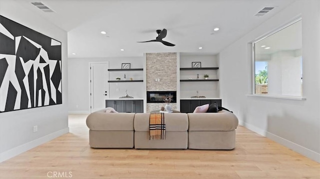 living room featuring a stone fireplace, light hardwood / wood-style floors, and ceiling fan