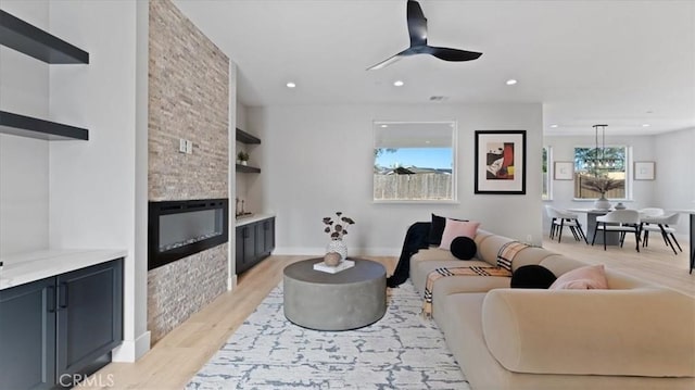 living room with built in shelves, a fireplace, light hardwood / wood-style floors, and ceiling fan