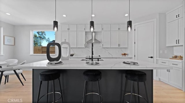 kitchen with an island with sink, hanging light fixtures, and white cabinets